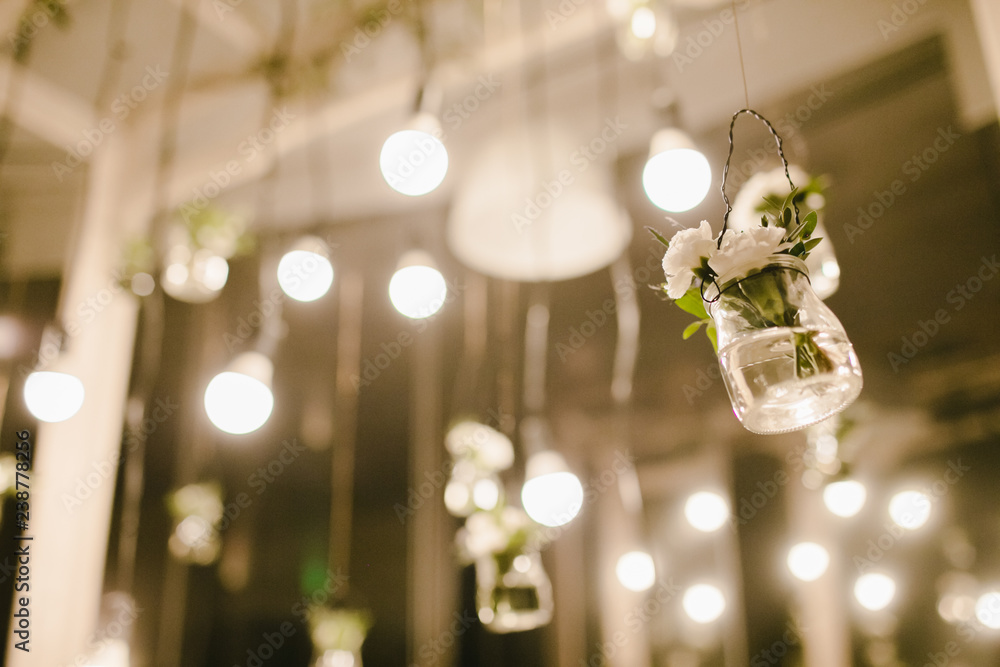 Light bulbs and little glasses with flowers hang from the ceiling as a part of wedding decor