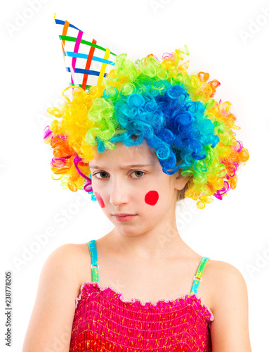 Portrait of little sad girl in clown wig and birthday hat with red spots on her cheeks isolated on white background
