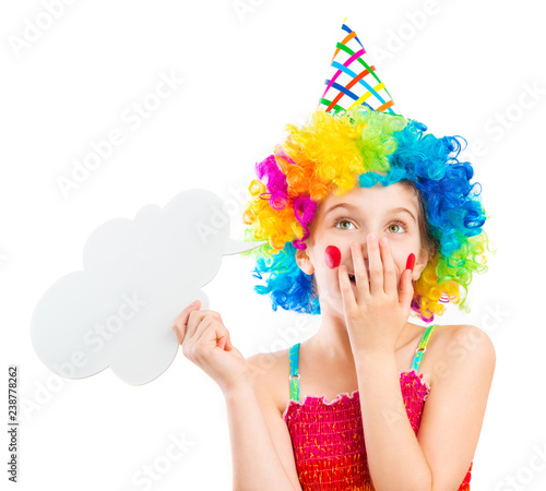 Lively little girl in bright colouful clown wig holding white speech bubble isolated on white background