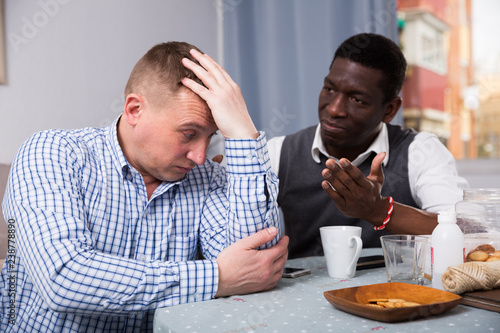 Upset man looking away after conflict, friend tries reconcile