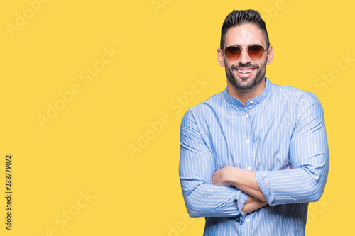 Young handsome man wearing sunglasses over isolated background happy face smiling with crossed arms looking at the camera. Positive person.