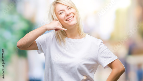 Young beautiful blonde woman wearing white t-shirt over isolated background smiling doing phone gesture with hand and fingers like talking on the telephone. Communicating concepts.