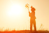 Little girl playing with wind toy or pinwheel against the sky at sunset. Happy girl silhouette