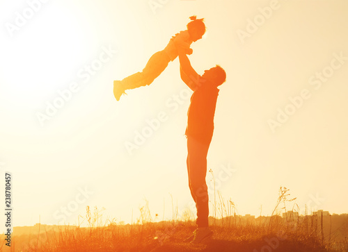 Silhouette of father throwing up his happy little daughter in the sky at sunset. Father and daughter playing in the frsh air. Happy family concept