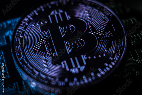 Bitcoin with bit symbol in blue light. Macro shot of physical bitcoin coin. Cryptocurrency, blockchain technology