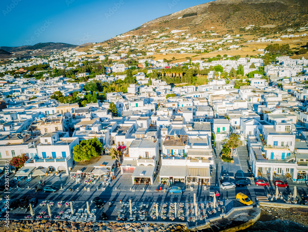 Fototapeta premium Cozy resort town by the seaside, Paros, Greece. Bird's eye view of traditional white houses at sunset