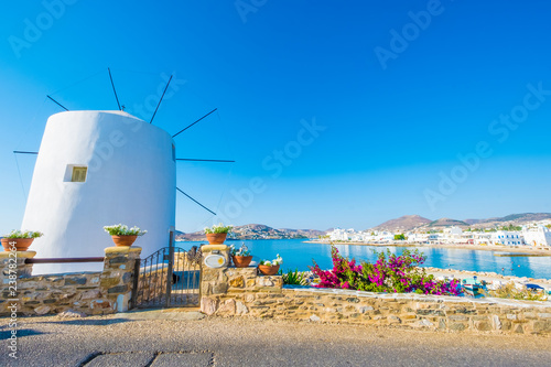 Fototapeta Naklejka Na Ścianę i Meble -  Old white windmill on the cliff in front of water and beautiful blue sky at sunny day, Paros, Greece
