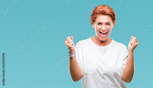 Atrractive senior caucasian redhead woman over isolated background celebrating surprised and amazed for success with arms raised and open eyes. Winner concept.