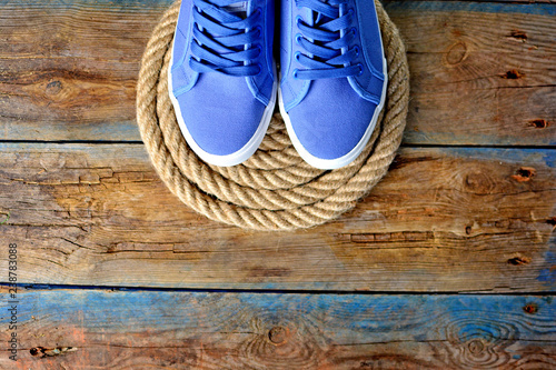 Blue sneakers shoes on a rope spiral, on a wooden weathered terrace. Yacht style concept. Template for avdertisement banner. photo