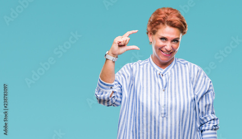 Atrractive senior caucasian redhead woman over isolated background smiling and confident gesturing with hand doing size sign with fingers while looking and the camera. Measure concept.