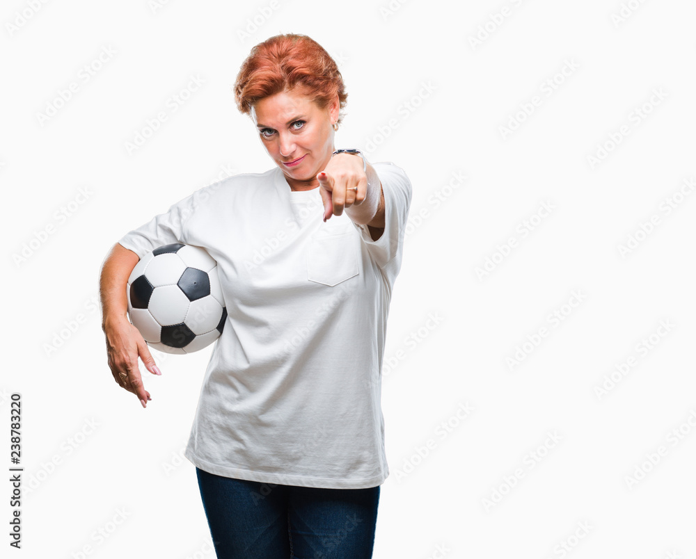 Atrractive senior caucasian redhead woman holding soccer ball over isolated background pointing with finger to the camera and to you, hand sign, positive and confident gesture from the front