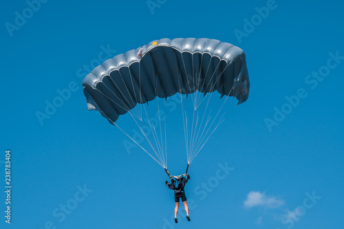 Skydiver with grey parachute in blue sky