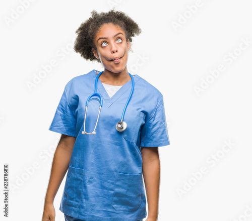 Young afro american doctor woman over isolated background making fish face with lips, crazy and comical gesture. Funny expression.