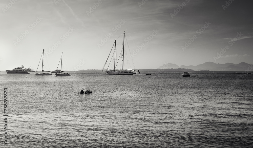 Black and white picture of the yachts and sailboats at anchor in Golfe Juan at the French beach resort of Juan-les-Pins with the island Ile Sainte-Marguerite in the background