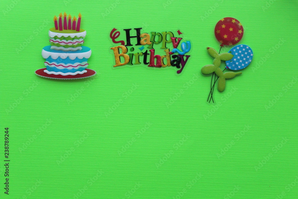 happy birthday written with different colors with a cake candles and balloons on a green background with writing space