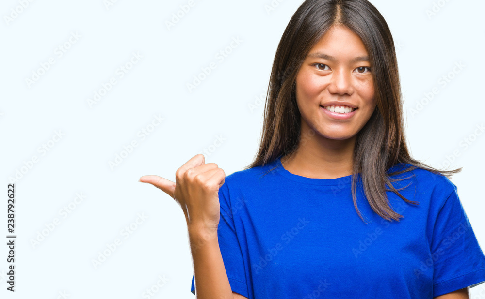 Young asian woman over isolated background smiling with happy face looking and pointing to the side with thumb up. Young asian woman over isolated background smiling with happy face looking and pointing to the side with thumb up.