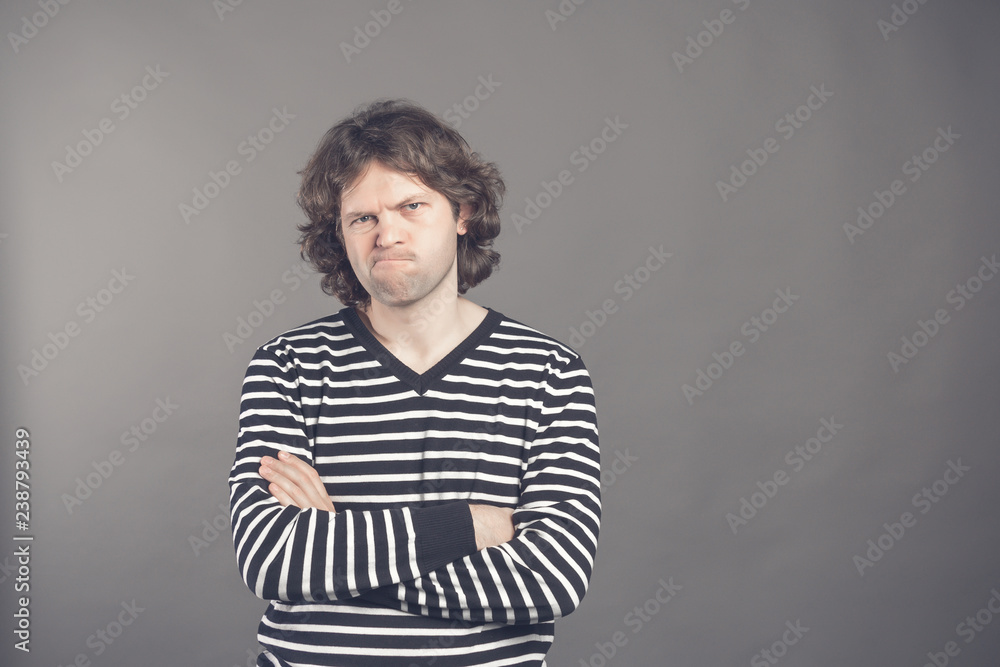 Closeup portrait, displeased, angry grumpy man in striped sweater bad attitude, arms crossed, folded, looking at you, isolated gray background. Negative human emotion, facial expression, feeling Closeup portrait, displeased, angry grumpy man in striped sweater bad attitude, arms crossed, folded, looking at you, isolated gray background. Negative human emotion, facial expression, feeling
