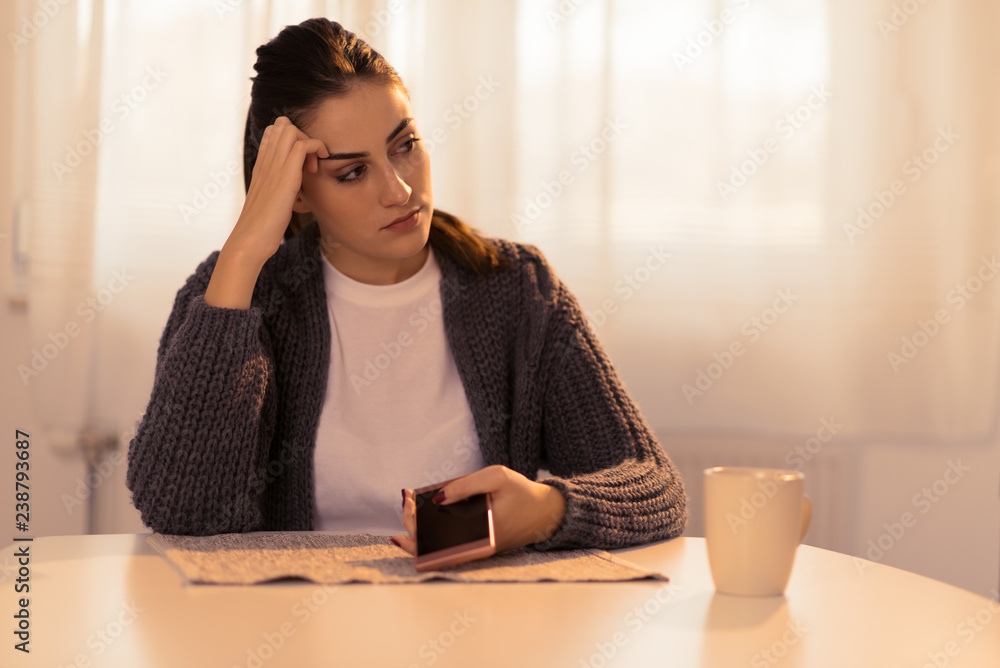 Depressed woman sitting at home and looking away while waiting for a call from her boyfriend Depressed woman sitting at home and looking away while waiting for a call from her boyfriend
