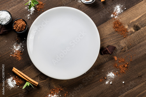 Empty white plate on dark wood, chocolate composition, aerial view