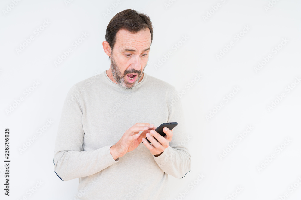 Senior man using smartphone over isolated background scared in shock with a surprise face, afraid and excited with fear expression Senior man using smartphone over isolated background scared in shock with a surprise face, afraid and excited with fear expression