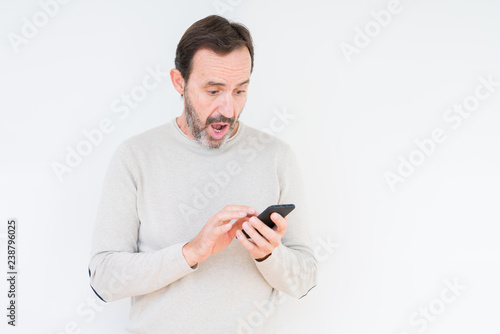 Senior man using smartphone over isolated background scared in shock with a surprise face, afraid and excited with fear expression © Krakenimages.com
