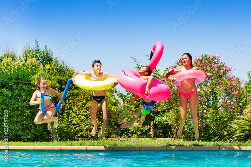 Four happy friends jumping into the swimming pool