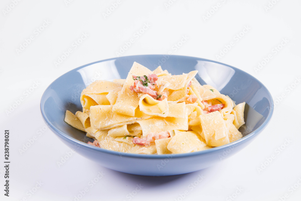 Pappardelle Carbonara on a blue plate on a white background