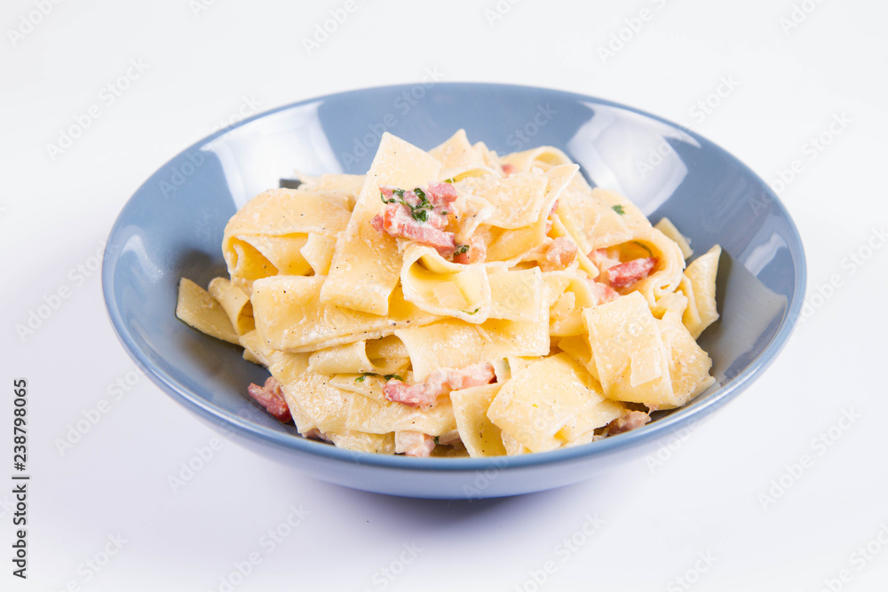 Pappardelle Carbonara on a blue plate on a white background