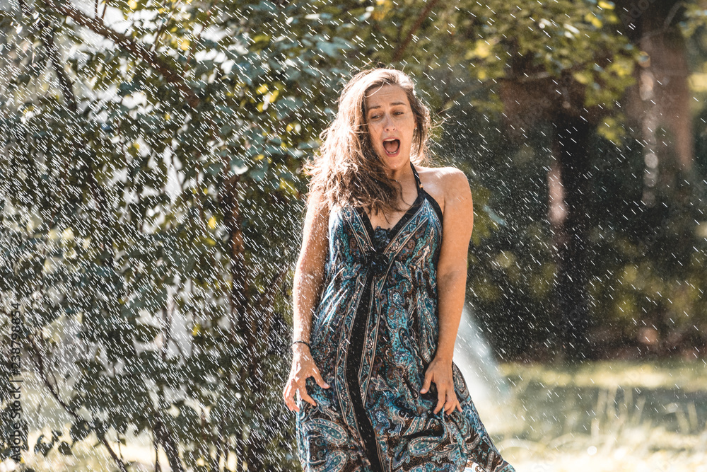 Girl being surprised by automatic watering and being wet in street or park. Girl in the rain having fun with cold water Girl being surprised by automatic watering and being wet in street or park. Girl in the rain having fun with cold water
