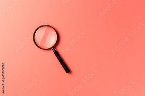 Magnifying glass on coral background. Top view. Flat lay. Copy space. New minimal creative concept. Living Coral color of the Year 2019