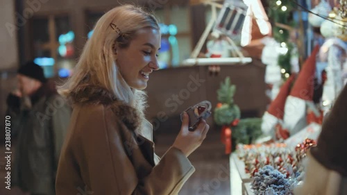Young blonde girl having fun at christmas market in a city. Happy attractive woman in a christmas market at night. Beautiful bokeh lights background.