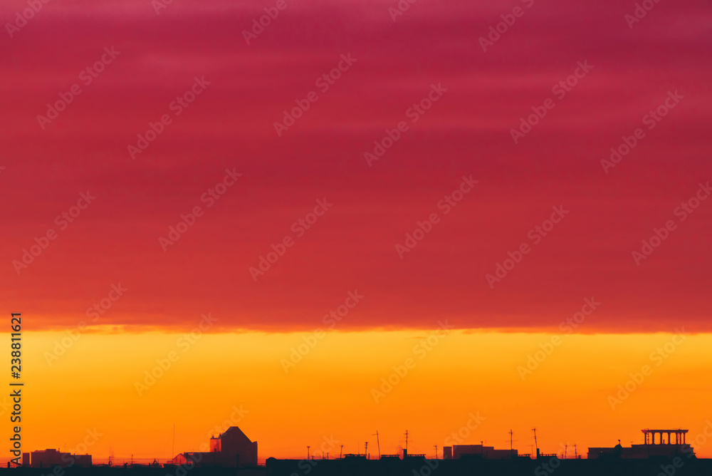 Cityscape with vivid surrealistic dawn. Amazing warm dramatic cloudy sky above dark silhouettes of city buildings. Orange sunlight. Atmospheric background of sunrise in overcast weather. Copy space.