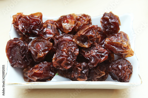 Black plum black plum dry in the plate . Prunes in a square white bowl on a white background. Prunes are the dried fruit group . Raisin in the bowl on the wood background