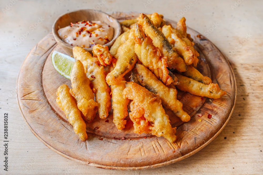 Deep fried whitebait sprats served in a crispy golden batter on a wooden platter serving board with a slice of lime and a small dish of chilly sauce as a dip Deep fried whitebait sprats served in a crispy golden batter on a wooden platter serving board with a slice of lime and a small dish of chilly sauce as a dip