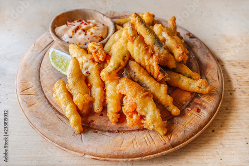 Deep fried whitebait sprats served in a crispy golden batter on a wooden platter serving board with a slice of lime and a small dish of chilly sauce as a dip photo