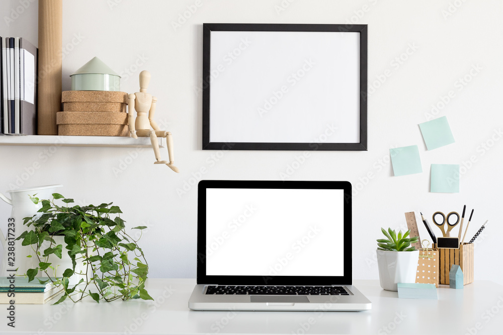 Fototapeta premium Laptop and poster frame on white wall in stylish home office. Mock up.