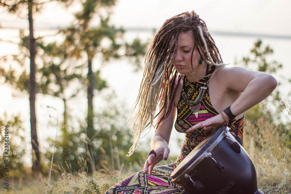 beautiful young woman hippie shaman playing djembe and dancing wild dances  at sunset Stock Photo