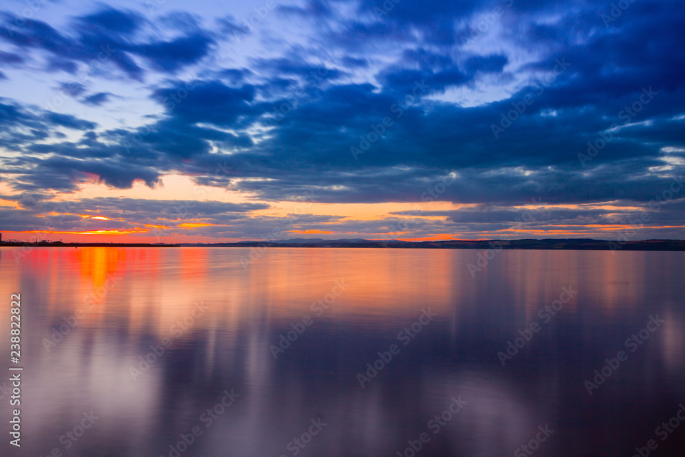 Fototapeta premium Dramatic colorful vibrant sunset sky with clouds reflected in the water