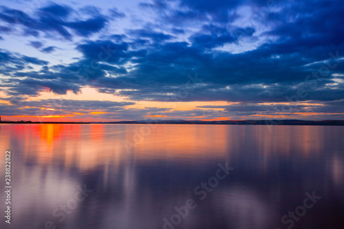 Dramatic colorful vibrant sunset sky with clouds reflected in the water