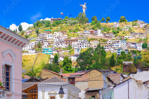 Outdoor view of colonial buildings houses located in the city of Quito with the statue of Virgin of Panecillo in the background in gorgeous sunny day with blue sky