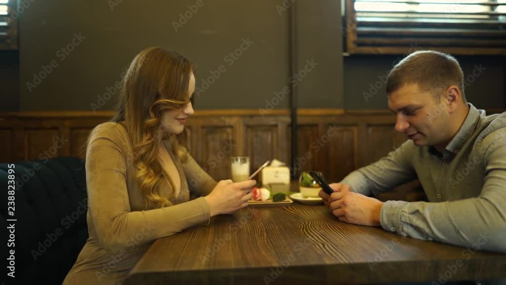 Couple sitting opposite each other in cozy cafe under wood table