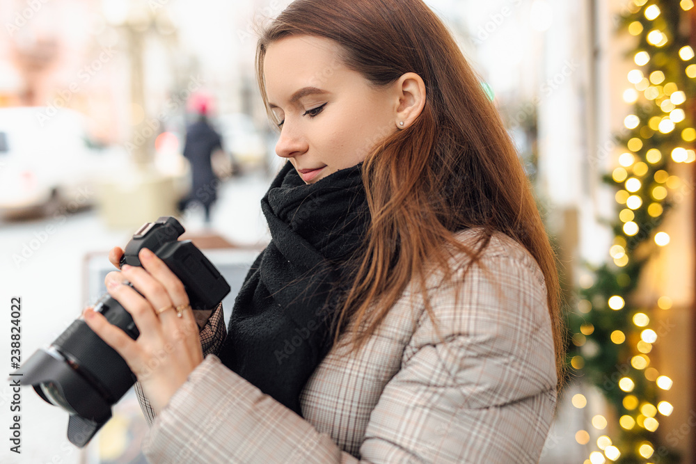 Photographer girl walk in the street and take photos in camera with happy face. Wear black scarf. Winter, autumn outfit.