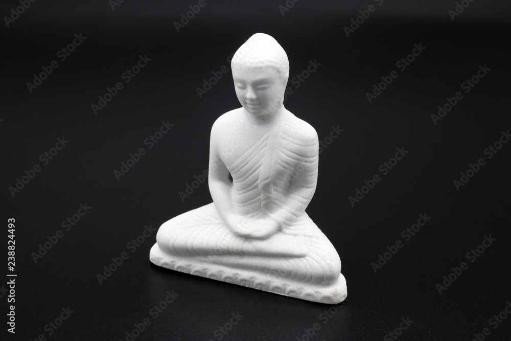 Ceramic statuette of white meditating buddha on a black background Ceramic statuette of white meditating buddha on a black background