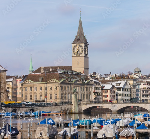 Buildings of the historic part of the Swiss city of Zurich along the Limmat river in winter, tower of the St. Peter Church above them, the Munsterbrucke bridge