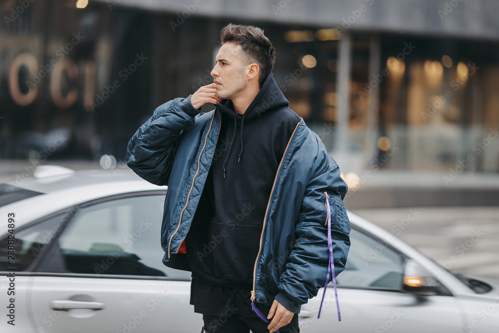 Fashionable man walk on the street near buildings. Wear blue jacket and all black. Winter, autumn outfit. Jacket with blouse and black sneakers.
