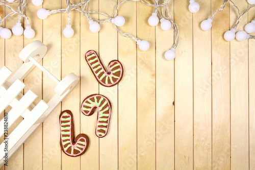 Tło - życzenia świąteczne - Boże Narodzenie - białe sanki i kolorowe pierniki z lampkami na jasnym tle