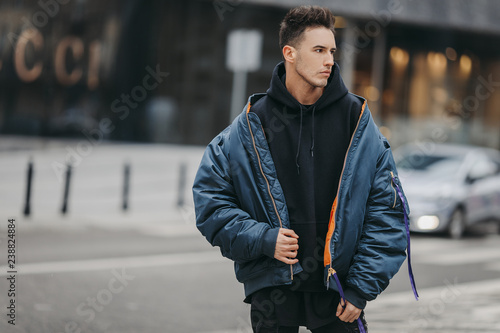 Fashionable man walk on the street near buildings. Wear blue jacket and all black. Winter, autumn outfit. Jacket with blouse and black sneakers. photo