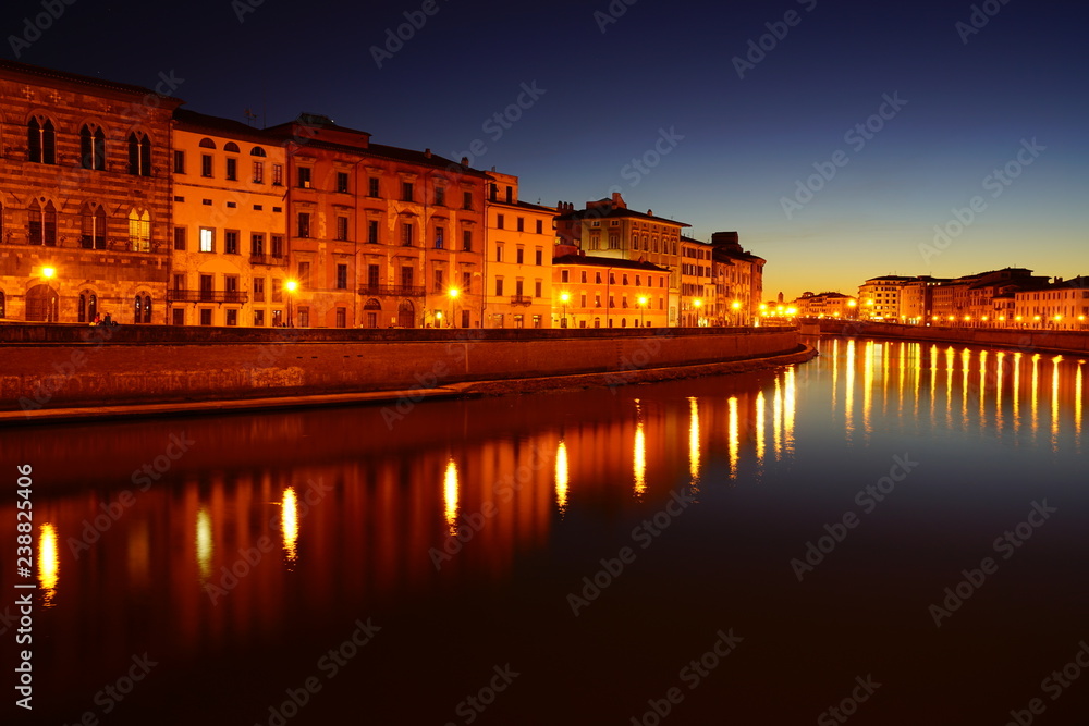 Night view of colorful medieval buildings on the quay reflecting on the Arno River in Pisa, Tuscany, Italy