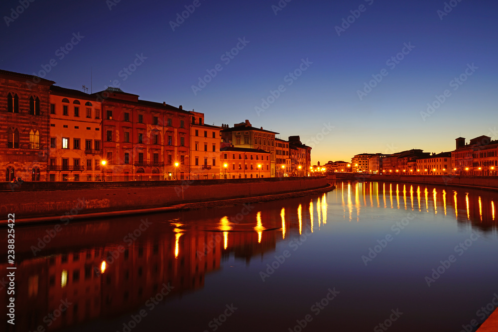 Night view of colorful medieval buildings on the quay reflecting on the Arno River in Pisa, Tuscany, Italy
