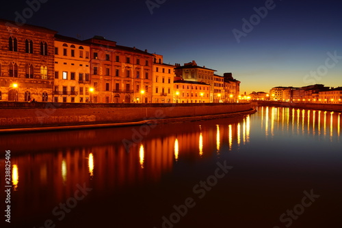 Night view of colorful medieval buildings on the quay reflecting on the Arno River in Pisa, Tuscany, Italy